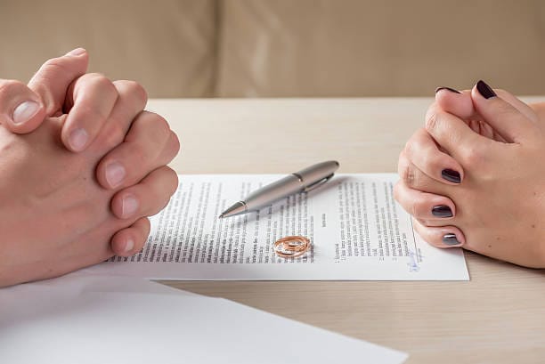 hands of wife and husband signing divorce documents or premarital agreement